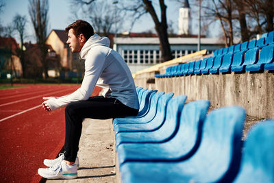 Man in sportswear resting at stadium seat after exercises