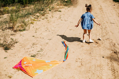 Rear view of a baby in a blue dress and a kite lying on a sandy road