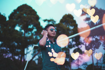 Man in sunglasses holding illuminated lights against sky