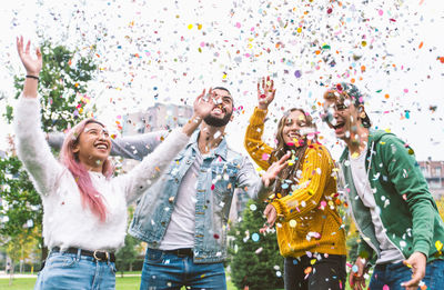 Cheerful friends throwing confetti while standing at park