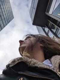 Low angle view of woman standing against sky and skyscrapers 