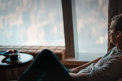 Side view of man sitting by window at home