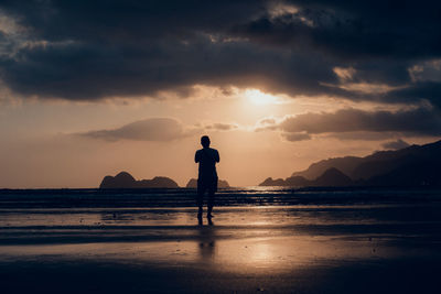 Silhouette man standing on beach against sky during sunset