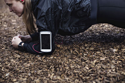 Side view of determined female athlete with smart phone in arm band performing plank position at forest