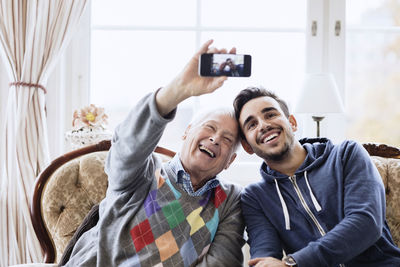 Happy senior man taking selfie with caretaker through smart phone at nursing home