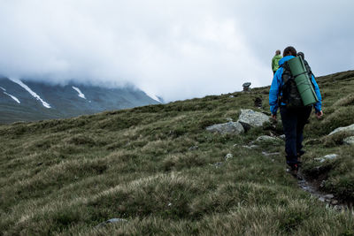 Rear view of women hiking on grassy mountain against sky