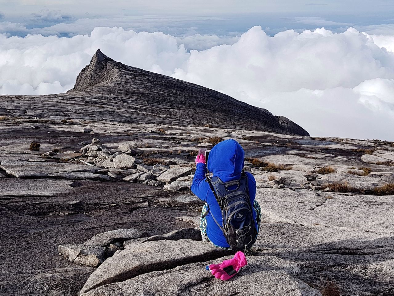 REAR VIEW OF PERSON ON ROCKS AGAINST SKY