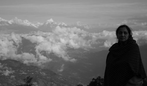 Woman wrapped in shawl standing on cliff against sky