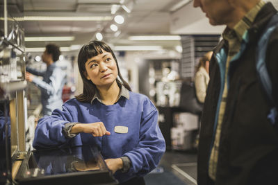 Saleswoman looking at mature customer while standing in electronics store