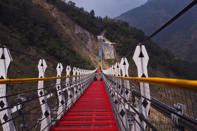 Footbridge amidst trees and mountains against sky