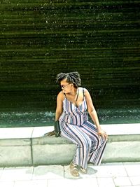 Young woman looking away while sitting against water fountain