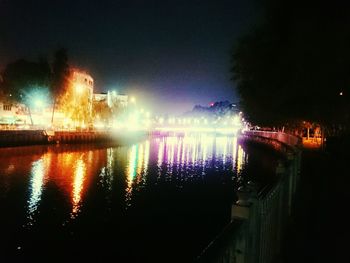Illuminated city by river against sky at night