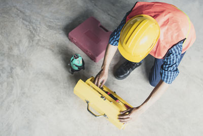 High angle view of architect removing tools from container while crouching on floor at construction site