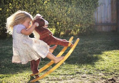 Side view of girl playing on rocking horse in yard