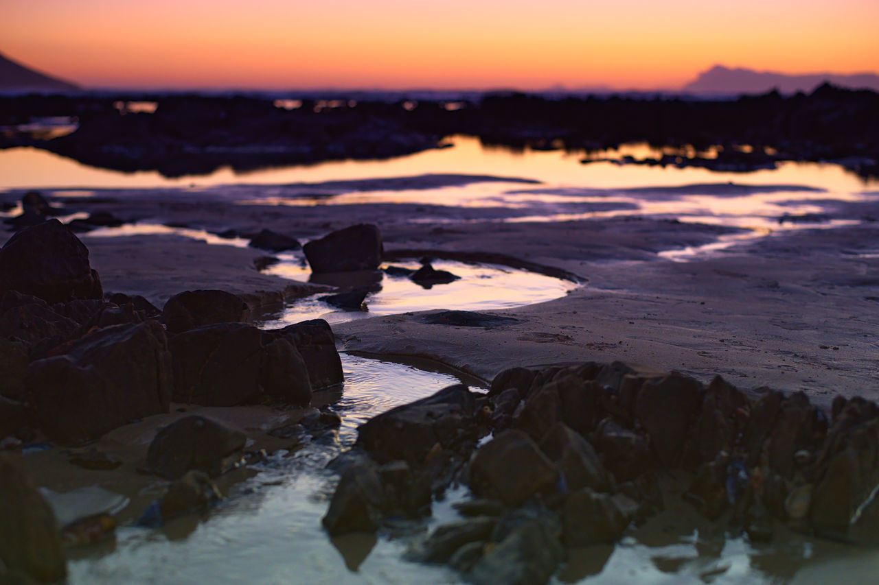 ROCKS ON SHORE AGAINST SKY DURING SUNSET