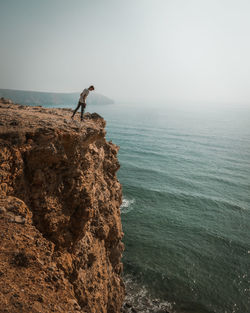 Man standing on rock by sea against sky