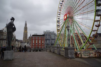 Ferris wheel in city against cloudy sky