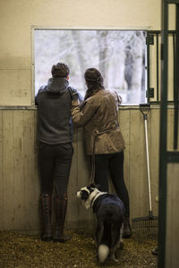 Full length rear view of young couple looking through window of horse stable