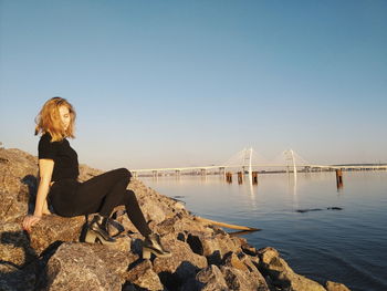 Woman sitting on bridge against clear blue sky