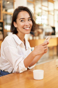 Portrait of young woman using mobile phone while sitting on table