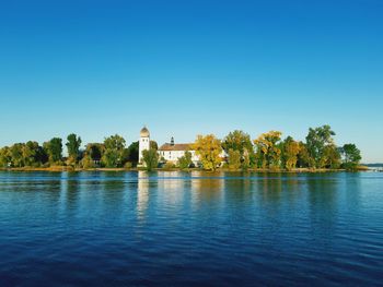 Scenic view of lake by building against clear blue sky