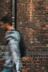 Blurred motion of man walking against brick wall