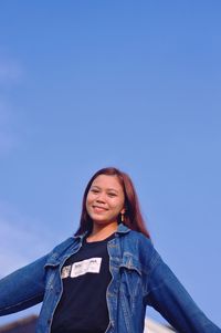 Portrait of young woman standing against clear blue sky