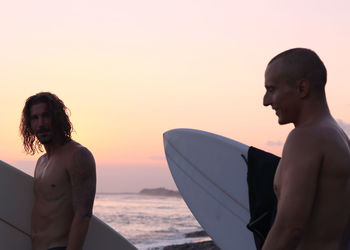 Man standing at beach against sky during sunset