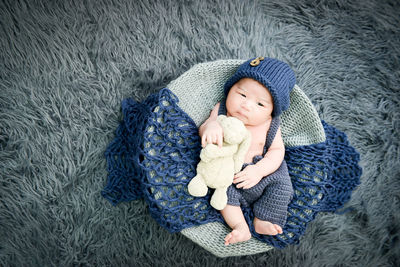 Directly above cute baby boy lying down in basket with stuffed toy on rug