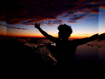 Silhouette person standing by sea against sky during sunset