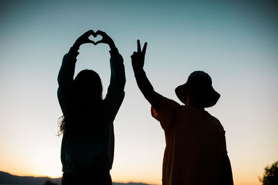 Love and peace sign silhouettes with colorful sky - young people