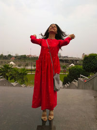 Full length of woman standing by red umbrella against sky