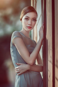 Portrait of young woman standing by against wall