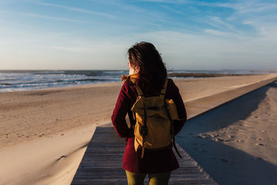 Rear view of woman standing on beach against sky