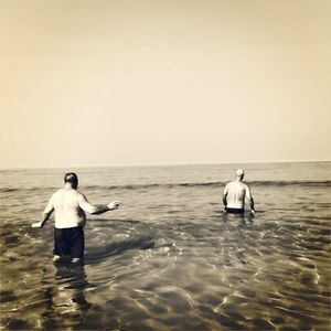 Rear view of men standing in sea against clear sky