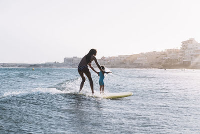 Pulled back view of mother and son surfing a small wave at sea