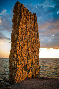 Sail rock on coastline of black sea against cloudy sky during sunset