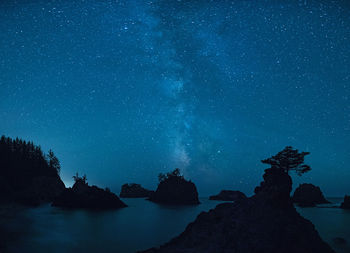 Scenic view of rock formations in sea against star field sky at night
