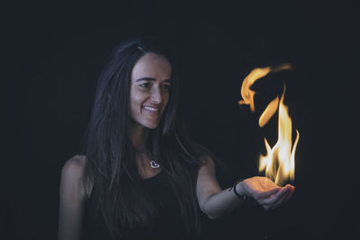 Portrait of young woman with fire against black background