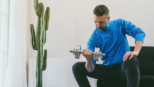 Sporty man working out and trains at home. fit boy doing exercises for biceps in the living room. 