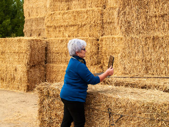 Side view of woman holding laptop against hay bales