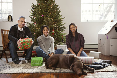 Happy family with dog sitting by christmas tree at home