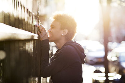 Cheerful young woman looking through railing during sunny day