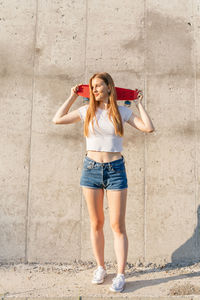 Happy teenage girl holding a skateboard over her head