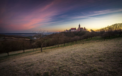 Scenic view of field and castle on a hill against sky during sunset