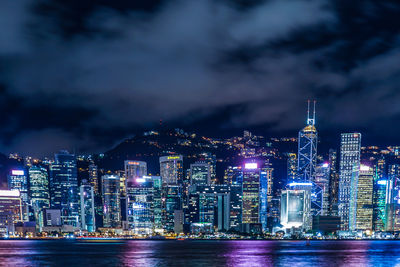 Illuminated city by sea against sky