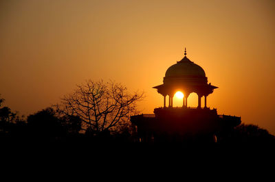 Silhouette tree by building against orange sky