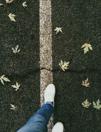 Low section of woman walking on road by fallen maple leaves during autumn
