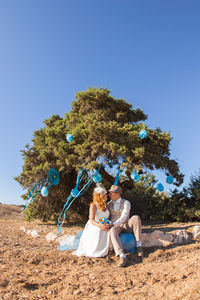 Couple sitting on tree against clear blue sky