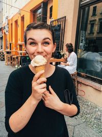 Portrait of happy young woman holding ice cream on sidewalk